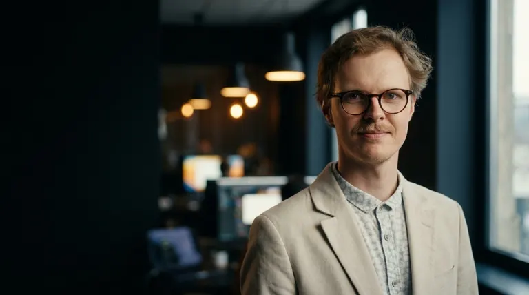 Jonas Blomgren i ljus kavaj och runda glasögon, i ett mörkt kontor